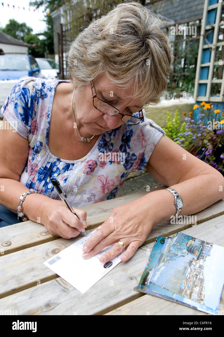 Une dame d'âge mûr écrit cartes postales de vacances Banque D'Images