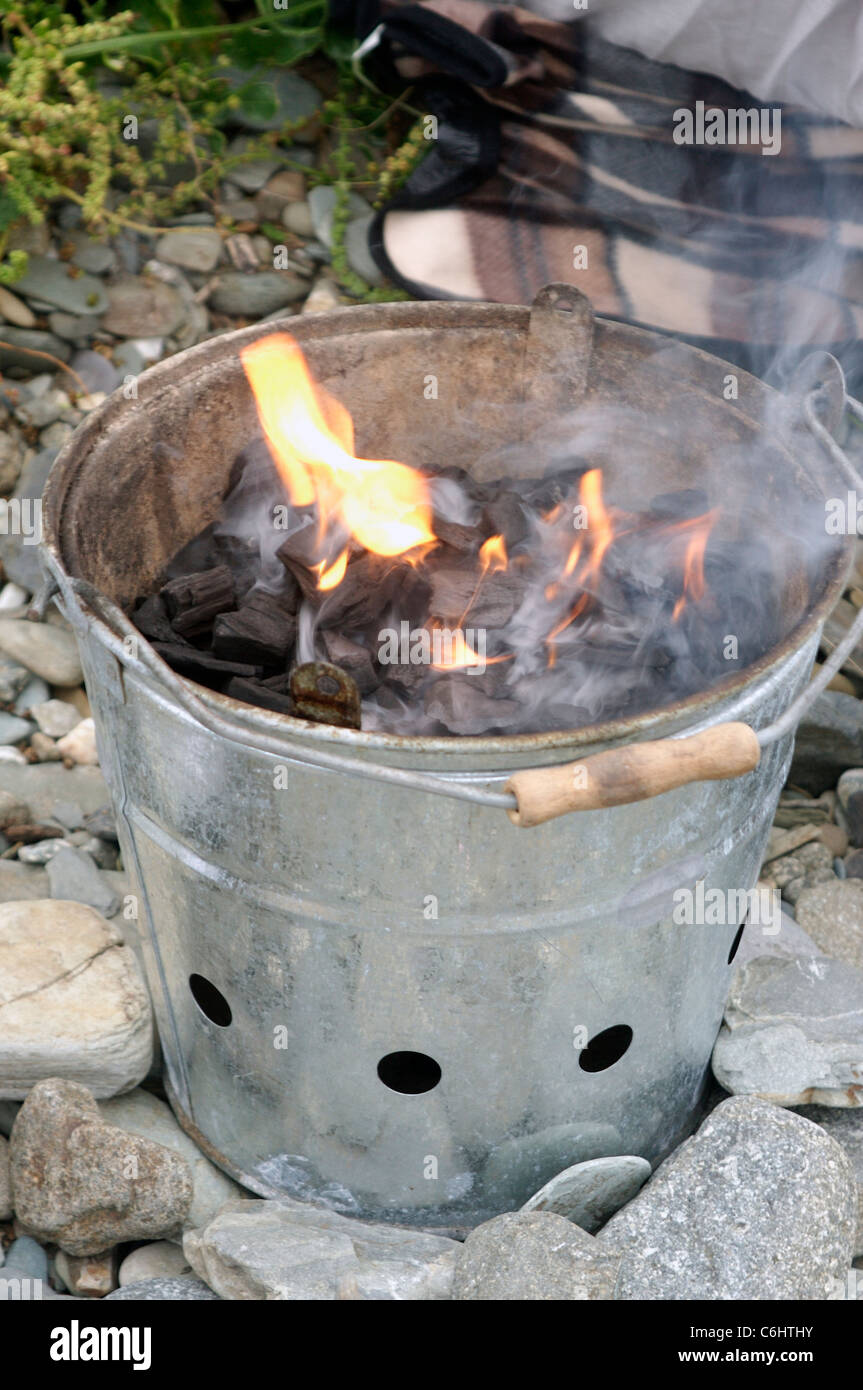 Le charbon de chauffe dans un petit barbecue sur une plage de rochers Banque D'Images