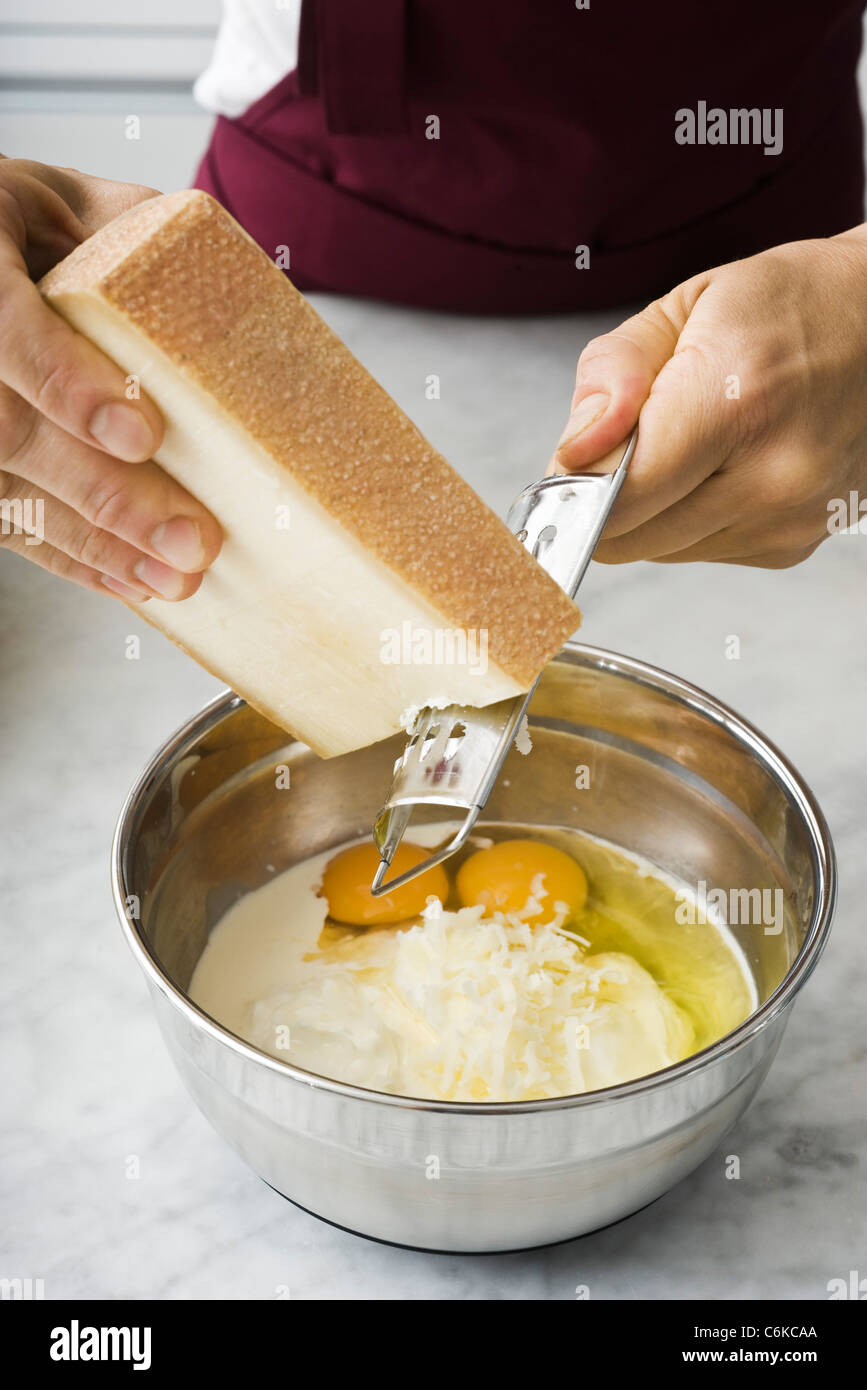 Râper le fromage dans le mélange d'œufs pour la quiche lorraine Banque D'Images