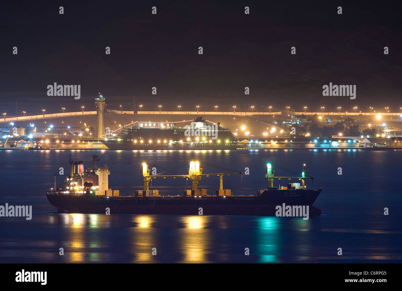 Un navire de vrac sec ancré dans la nuit. Dans l'arrière-plan : Mme 'Le Monde' amarré au port d'Aqaba, en Jordanie. Banque D'Images