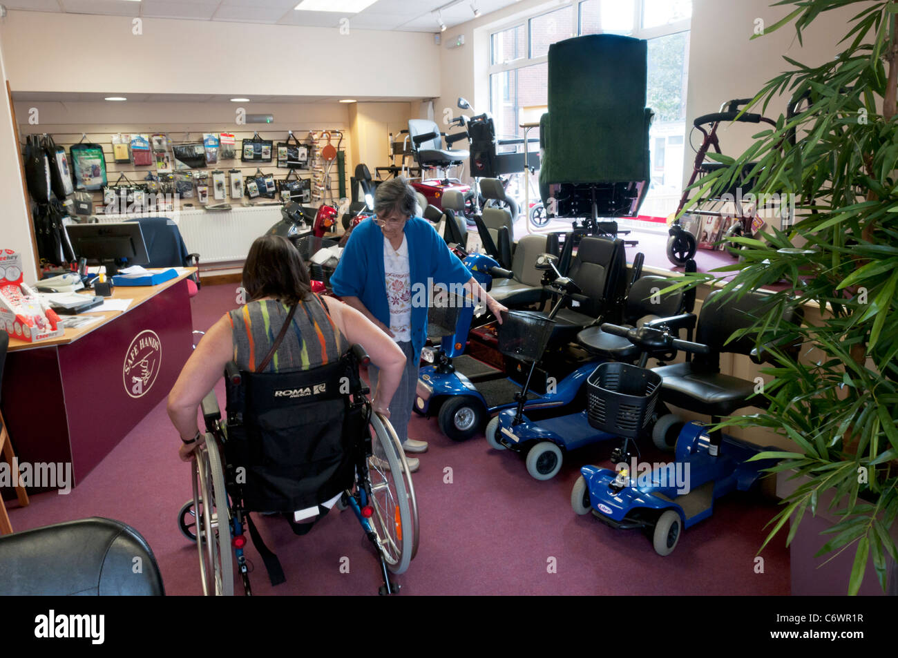 Une femme âgée et sa fille essayer un fauteuil roulant dans la salle d'exposition du Centre de mobilité des mains sûres, Birchington, Kent. Banque D'Images