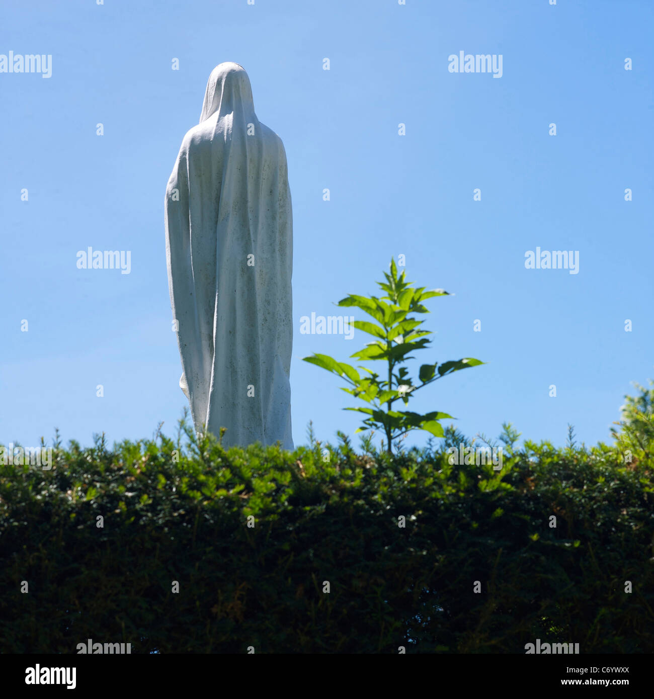 Statue d'une figure de la Vierge Marie en draperie blanche contre un ciel bleu clair dans un jardin serein Banque D'Images
