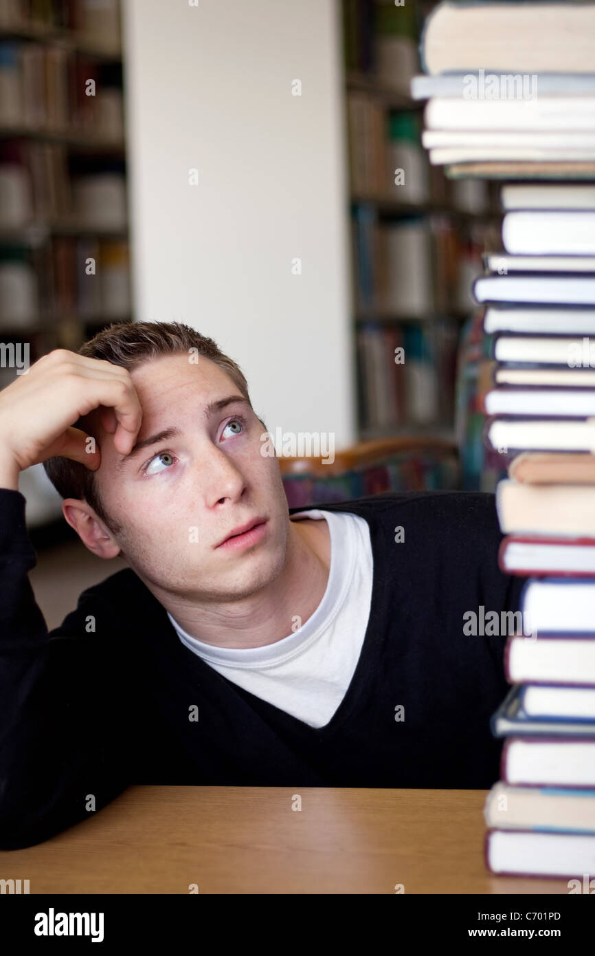 Un étudiant frustré et stressé regarde la haute pile de manuels qu'il a pour aller jusqu'à faire ses devoirs. Banque D'Images