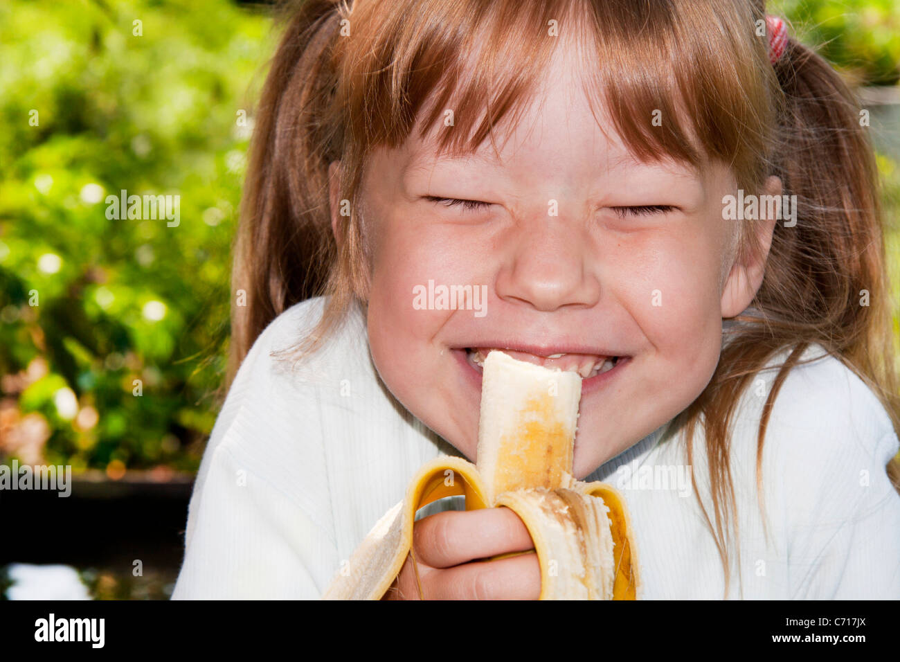 Petite fille dans l'extérieur mange une banane et rires Banque D'Images