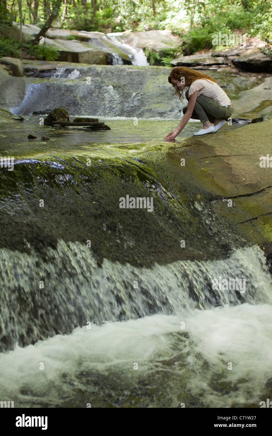 Femme accroupie à côté d'eau en cascade, plongeant les mains dans l'eau Banque D'Images