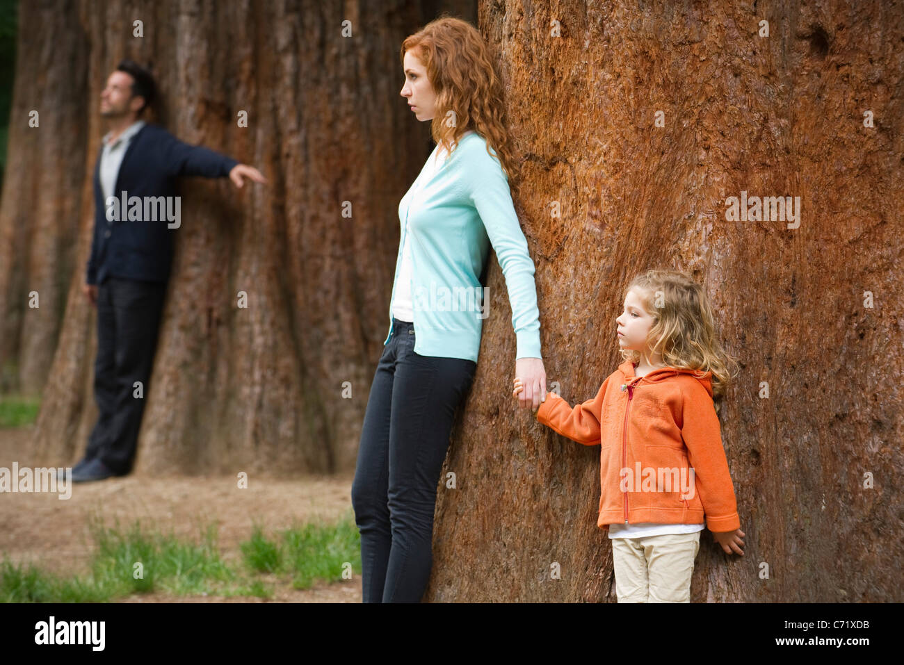 Mère et fille leaning against tree, père séparé debout en arrière-plan Banque D'Images