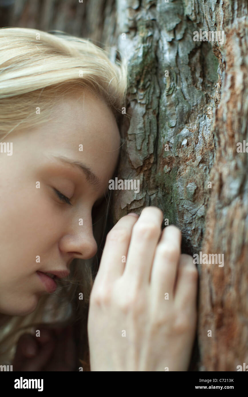 Young woman leaning forhead contre le tronc de l'arbre, les yeux fermés Banque D'Images