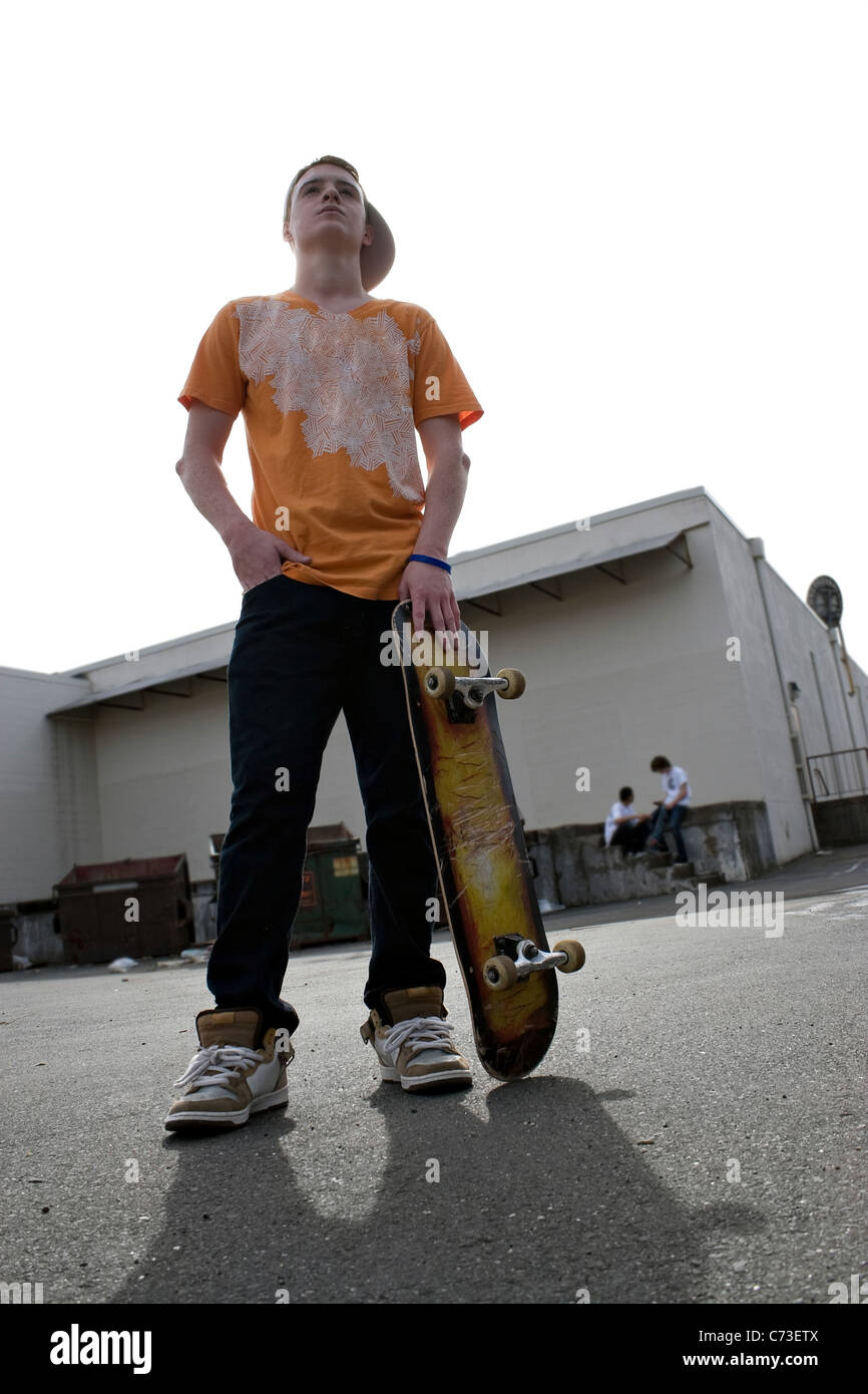 Un adolescent se tenant sur sa planche à roulettes skateboard et d'autres enfants traîner dans l'arrière-plan. Banque D'Images