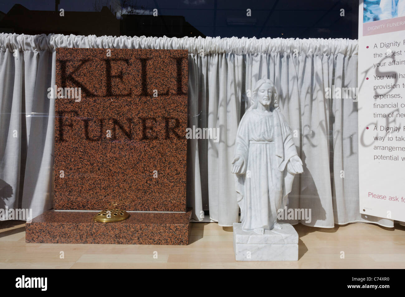 Une petite statuette de Jésus se tient en plein soleil dans un funérarium's fenêtre avant. Banque D'Images