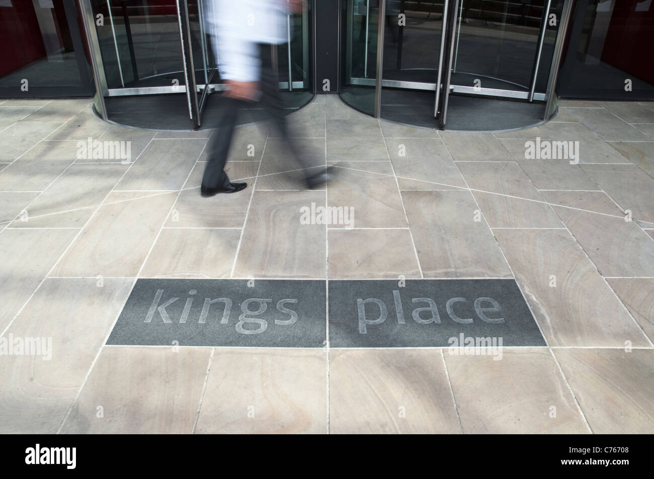 L'entrée de Kings Place à Londres, avec des portes tournantes, la figure floue d'un homme, et la construction d'un logo. Banque D'Images