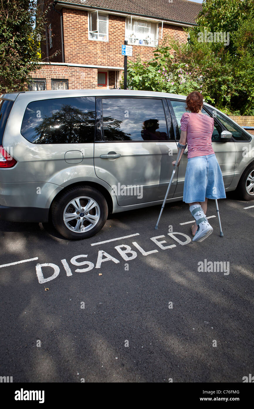 Femme avec jambe cassée le déverrouillage de porte de voiture garée dans un parking handicapés bay. Banque D'Images