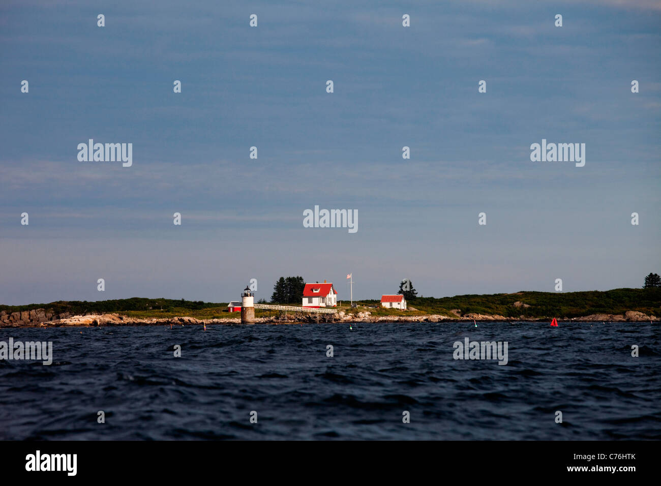 Un phare se tient dehors sous un ciel bleu et le bleu profond de l'eau. Banque D'Images