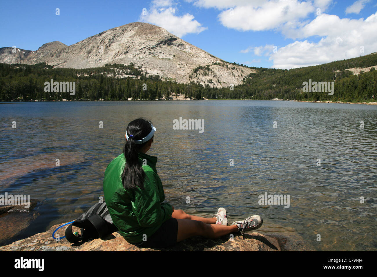 Horizontal image d'une femme dans une gaine verte est assis sur un rocher par Silas alpine Lake dans la gamme Wind River Banque D'Images
