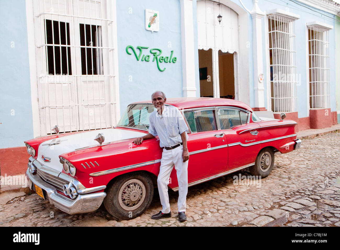 Homme debout en face de sa voiture américaine vintage rouge (Chevrolet) en face de la Via Reale, Trinidad, Sancti Spiritus, Cuba Banque D'Images