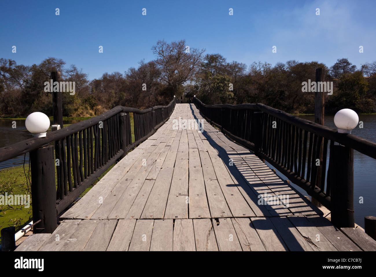 Un pont de bois sur une rivière avec des arbres et ciel bleu en arrière-plan Banque D'Images