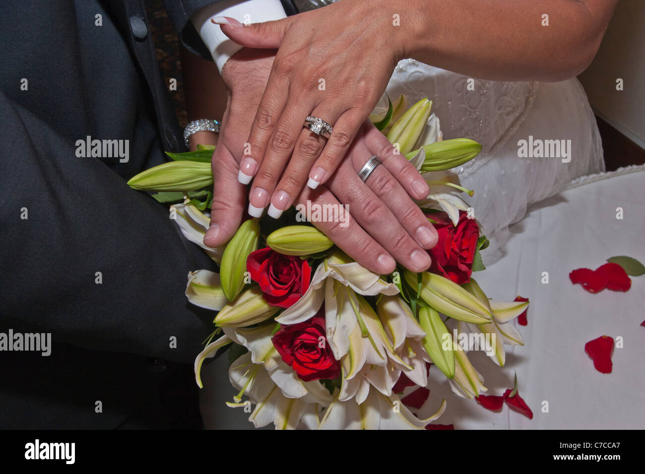 Jeune couple interracial nouvellement marié montrant leurs mains avec des bandes de mariage avec bouquet de mariage de mariées dans le fond haute résolution Banque D'Images