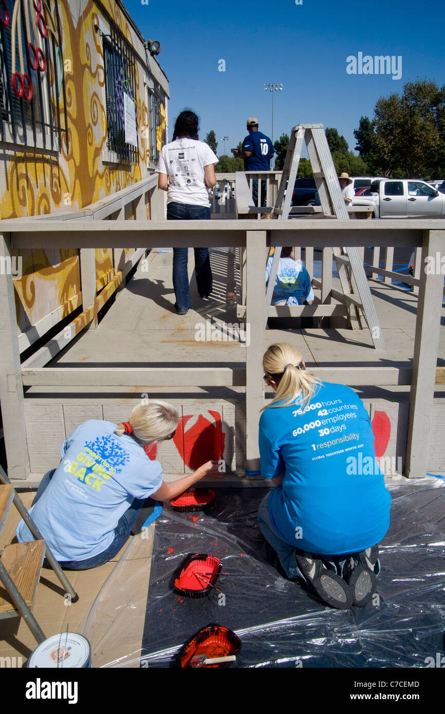 Deux jeunes femmes bénévoles peinture décorations sur un bâtiment de ville au cours d'un programme d'embellissement de la collectivité à Santa Ana, CA. Banque D'Images