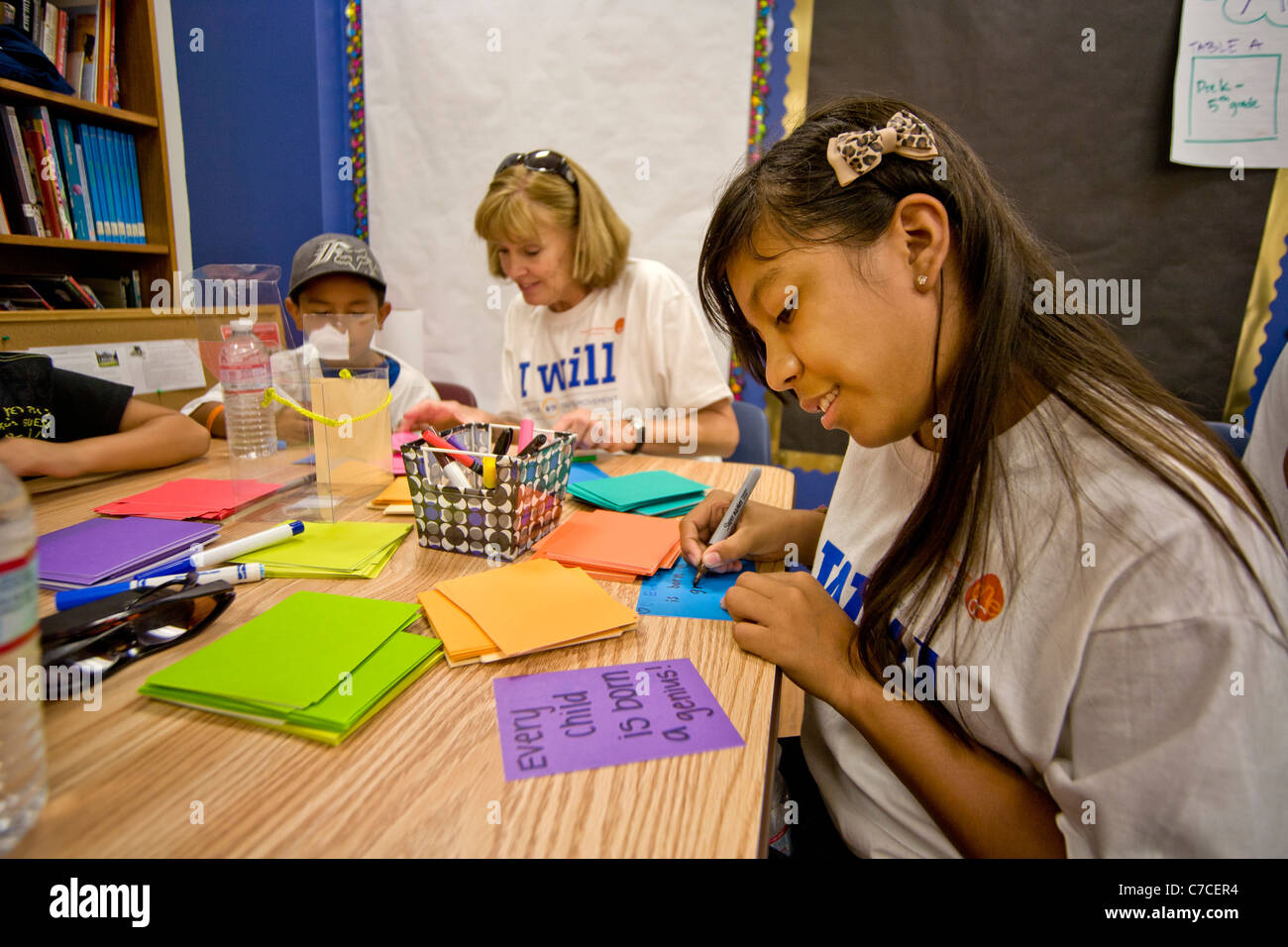 Un adolescent hispanique volontaire dans un Santa Ana, CA, middle school écrit notes encourageant pour les nouveaux étudiants. Remarque logo T-shirt. Banque D'Images