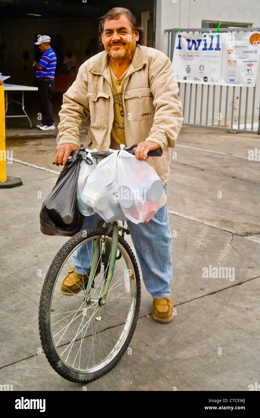 Un homme hispanique des dons alimentaires packs à un organisme de bienfaisance la distribution à Santa Ana, CA, à transporter accueil sur une bicyclette. Remarque la charité d'un logo. Banque D'Images