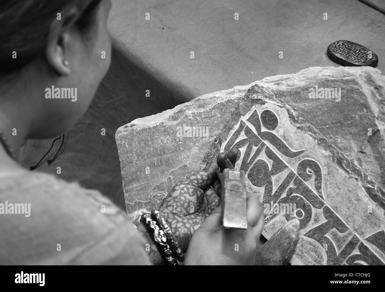 Une femme avec des mains décorées au henné sculpte la pierre en tibétain mani offres à Swayambunath, Katmandou, Népal Banque D'Images