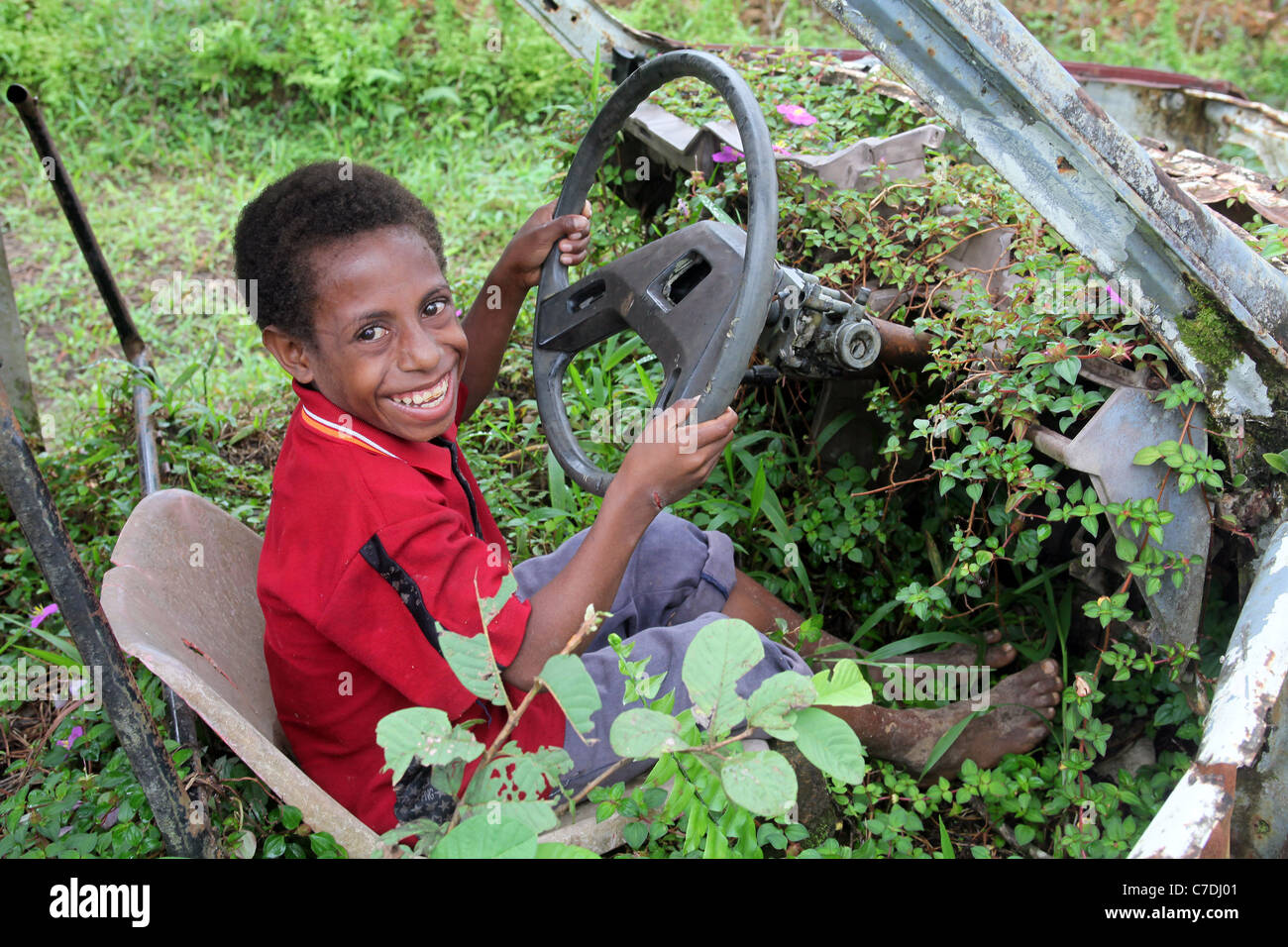 Garçon dans une carcasse de voiture rouillée envahie, Papouasie Nouvelle Guinée Banque D'Images