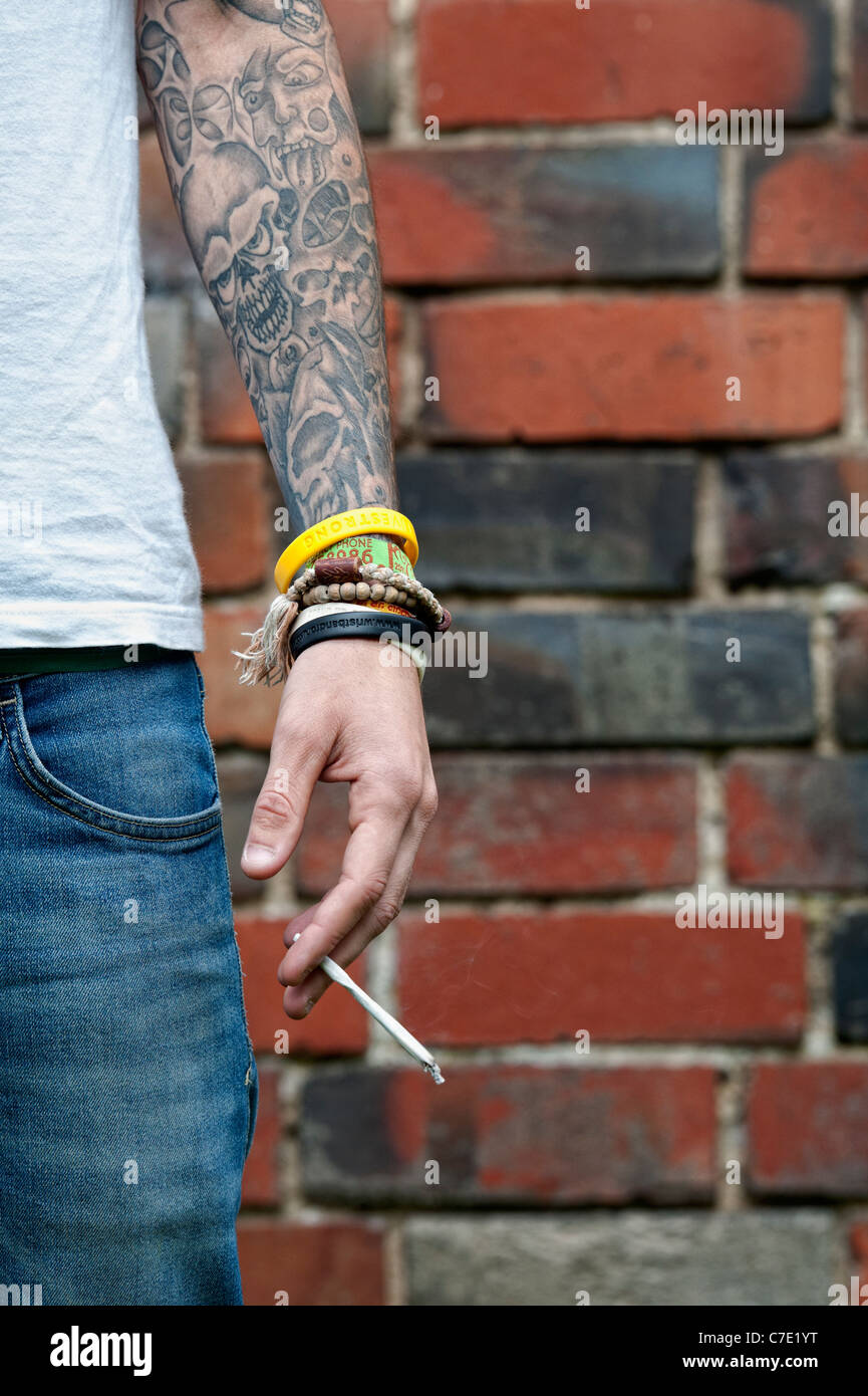 L'adolescent tatoué tenant un joint de cannabis Banque D'Images