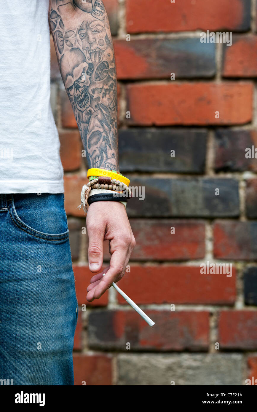 L'adolescent tatoué tenant un joint de cannabis Banque D'Images