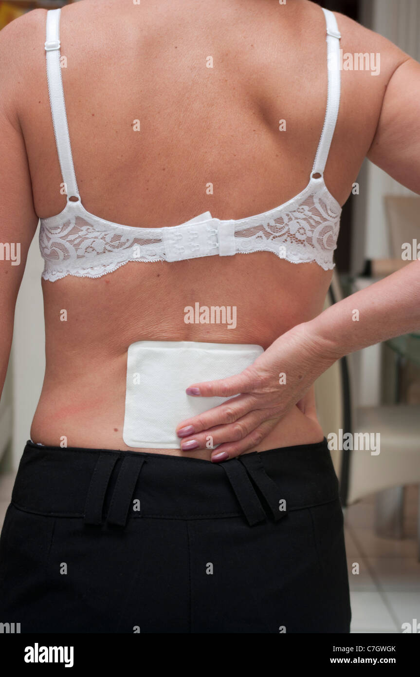 Personne Female Woman d'une douleur au dos portant un tampon de chaleur dans le bas du dos Banque D'Images