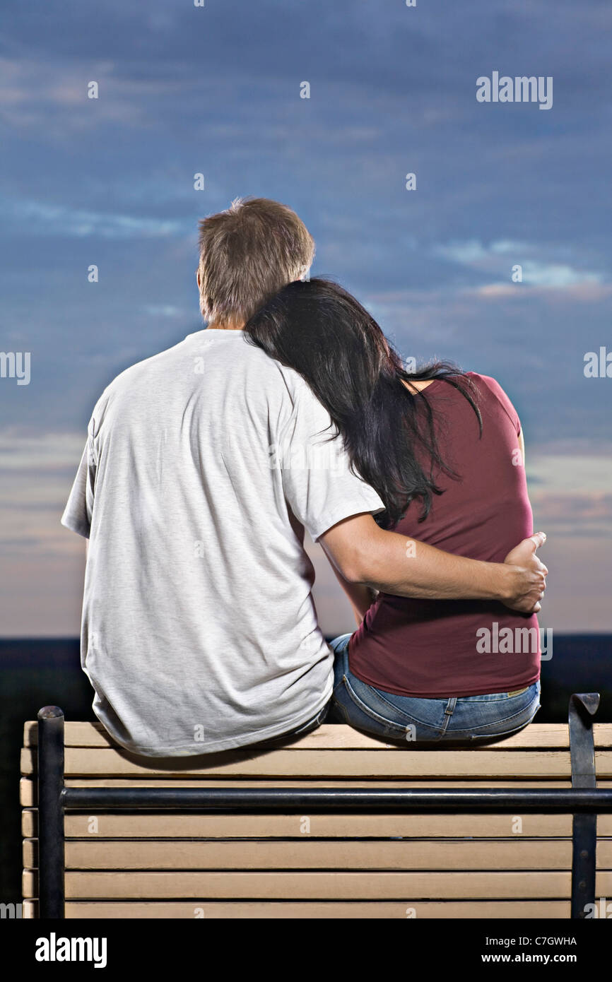 Un couple assis sur un banc, regardant le coucher de soleil Banque D'Images