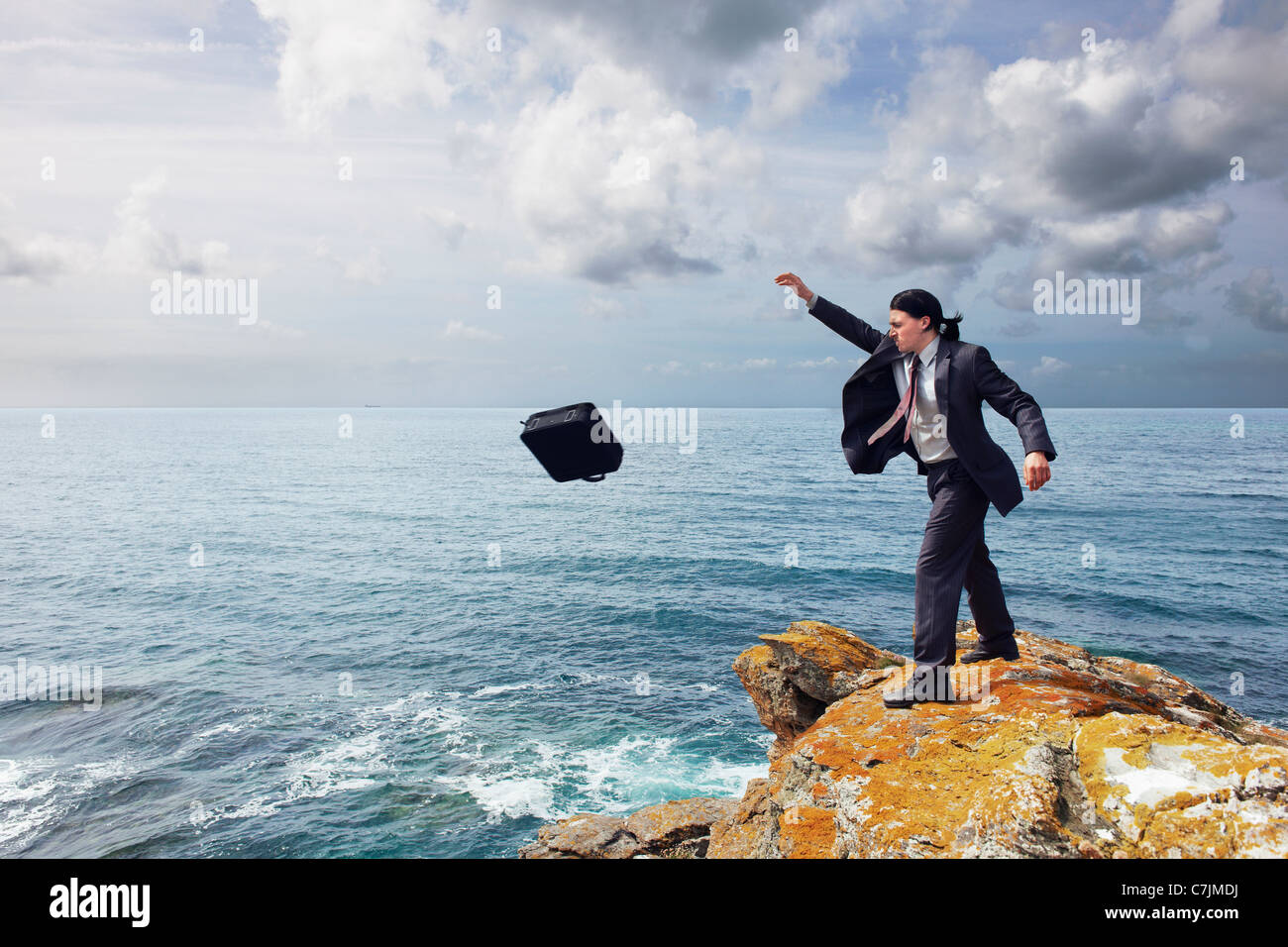 Businessman throwing briefcase off cliff Banque D'Images