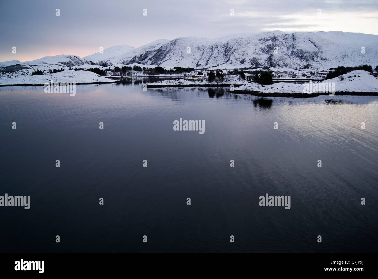 Fjord norvégien à l'aube avec ses montagnes couvertes de neige et mer calme. Banque D'Images