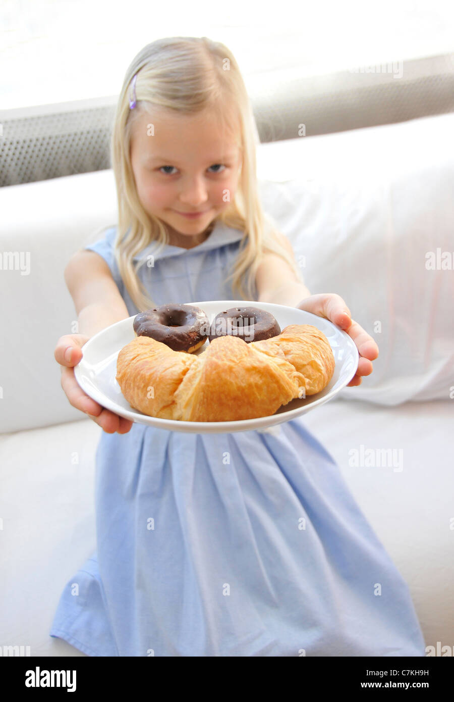 Jeune fille, 6, avec une robe bleue présentant une plaque avec des beignets au chocolat et un croissant Banque D'Images