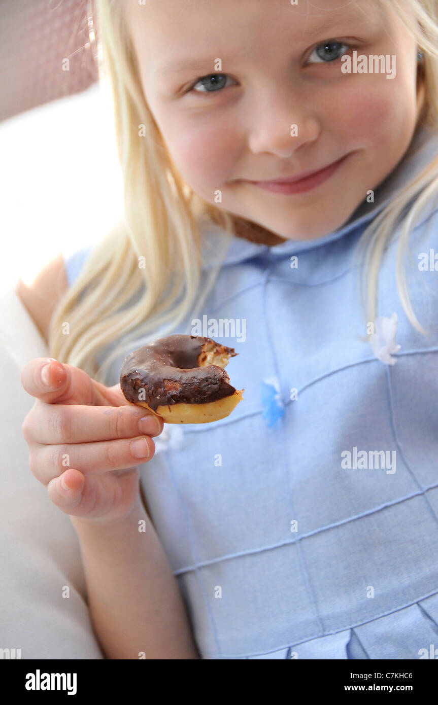 Jeune fille, 6, avec une robe bleue et un chocolat donut dans sa main Banque D'Images