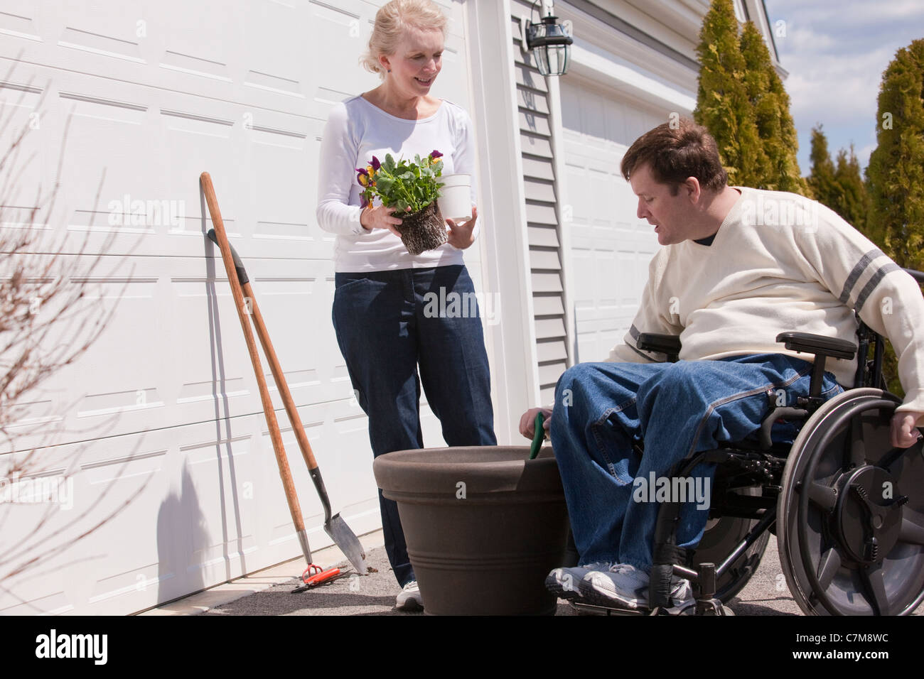 L'homme avec la moelle épinière planter des fleurs à l'extérieur de sa maison avec sa femme Banque D'Images