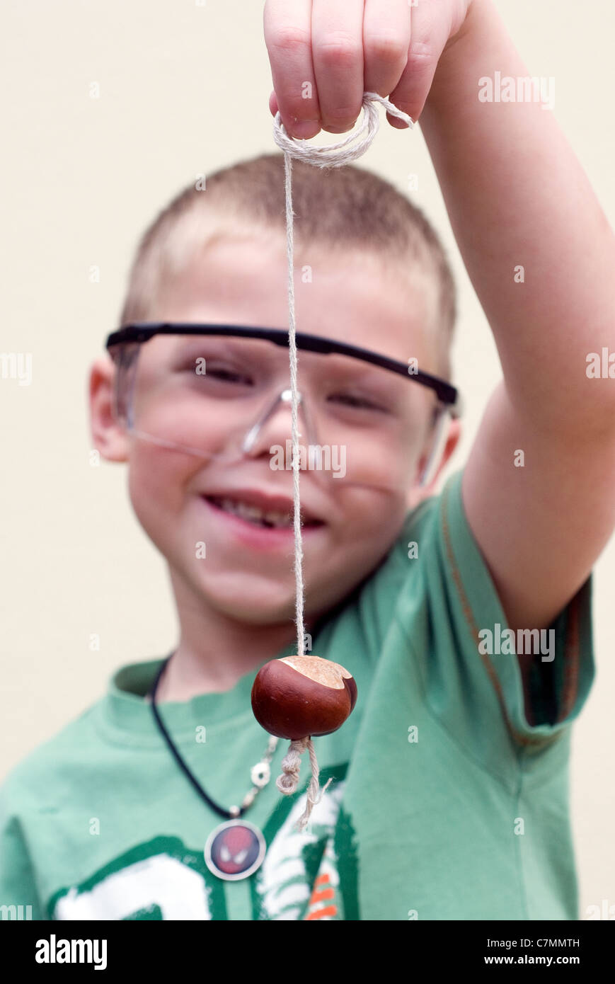 Boy playing Conkers avec des lunettes de sécurité, sur le châtaignier, conkers, décoration, jeu, holding, cheval, horse-chestnut, isolé, Banque D'Images