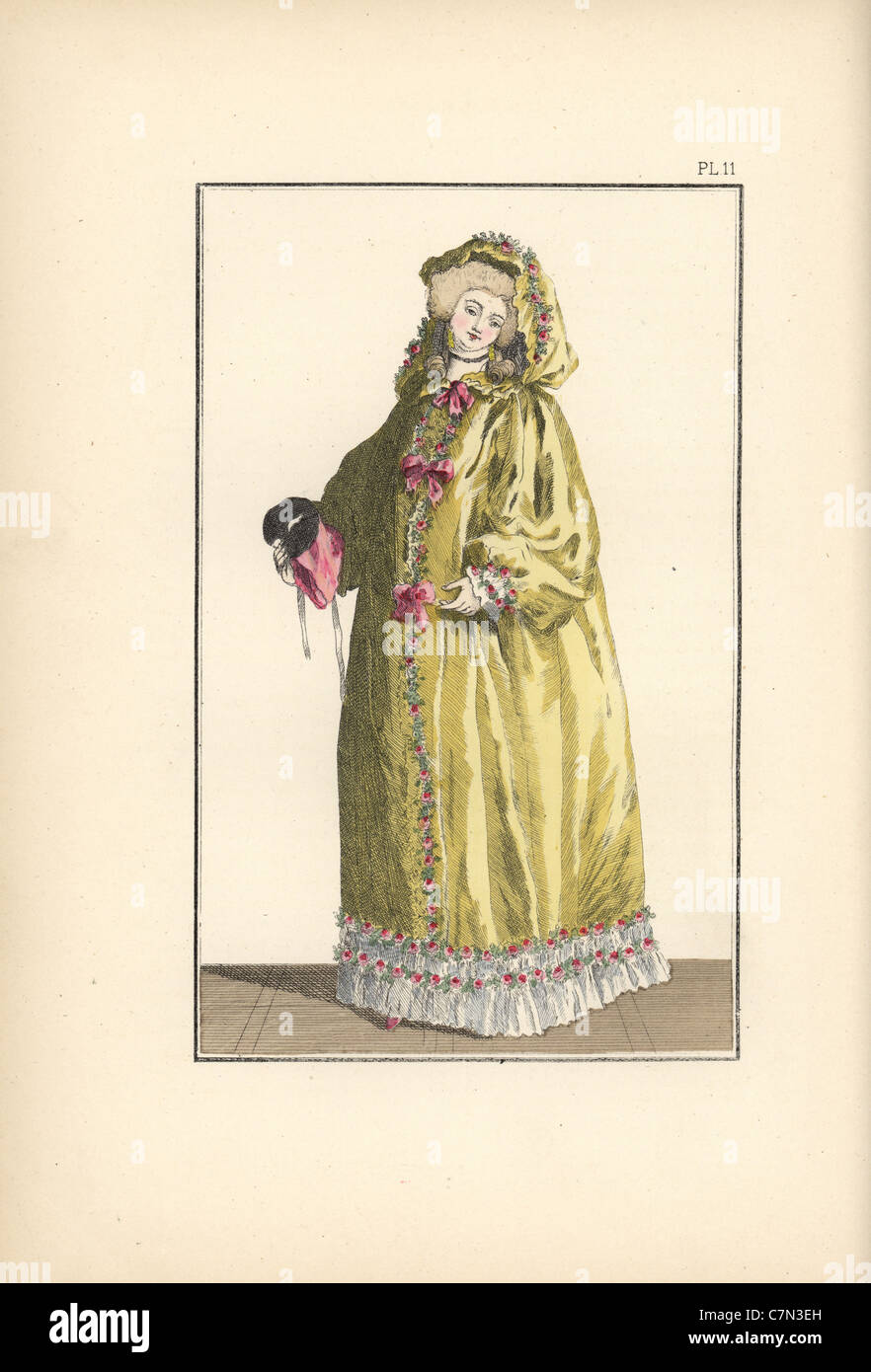 Femme en jaune canari cape à capuchon de taffetas garni de roses et de rubans, avec bar d'oreilles à billes et masque. Banque D'Images