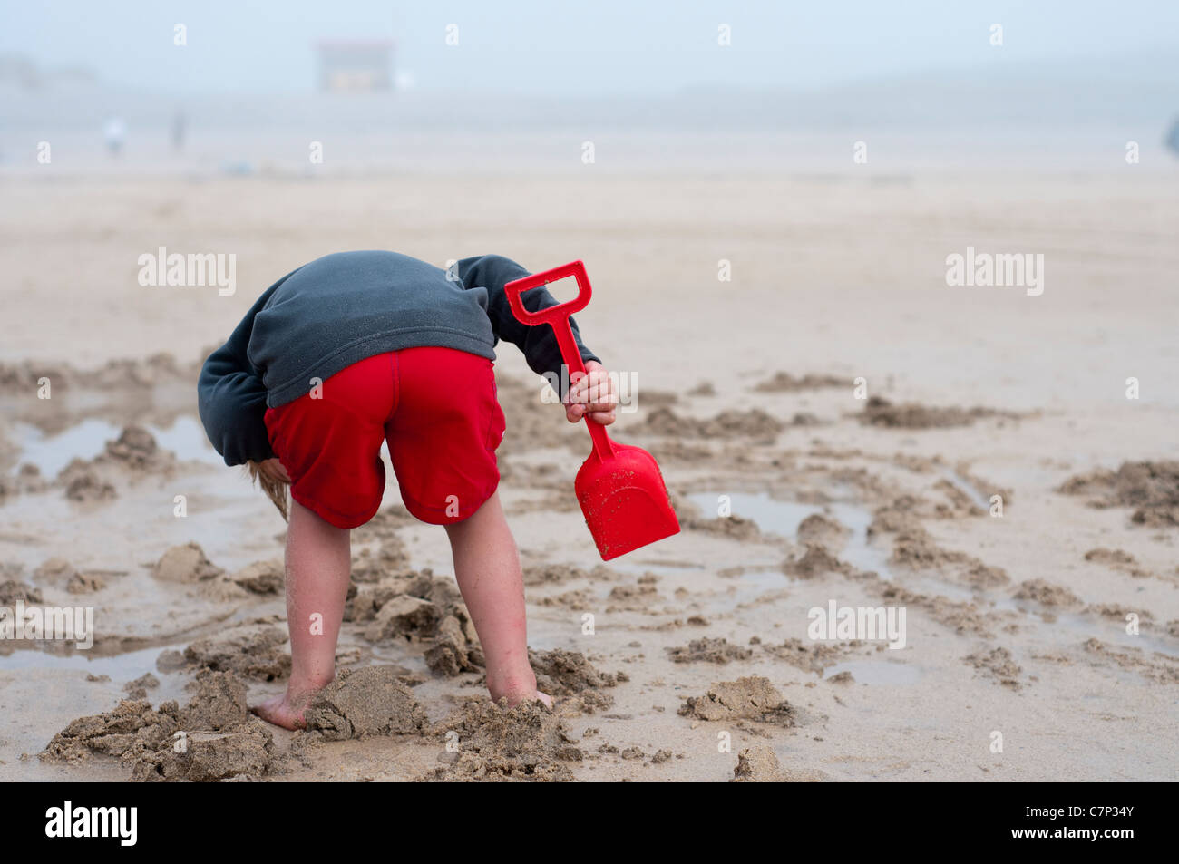Vue arrière du garçon en short rouge avec cosse rouge jouant dans le sable sur la plage en se penchant la construction d'un château de sable Banque D'Images