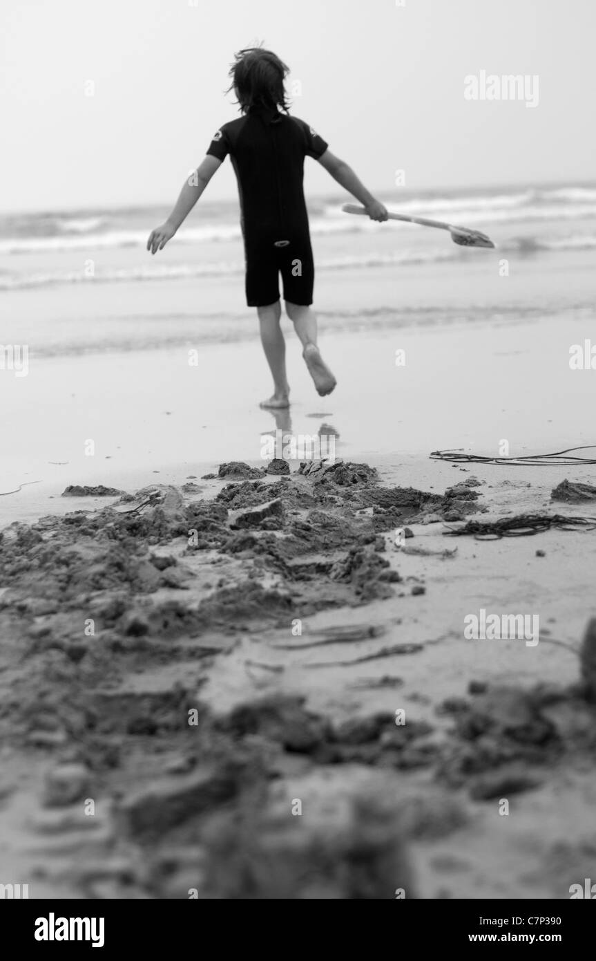 Boy running dans la mer avec son chat après avoir creusé un peu de sable. La station de vacances. Photographie noir et blanc Banque D'Images