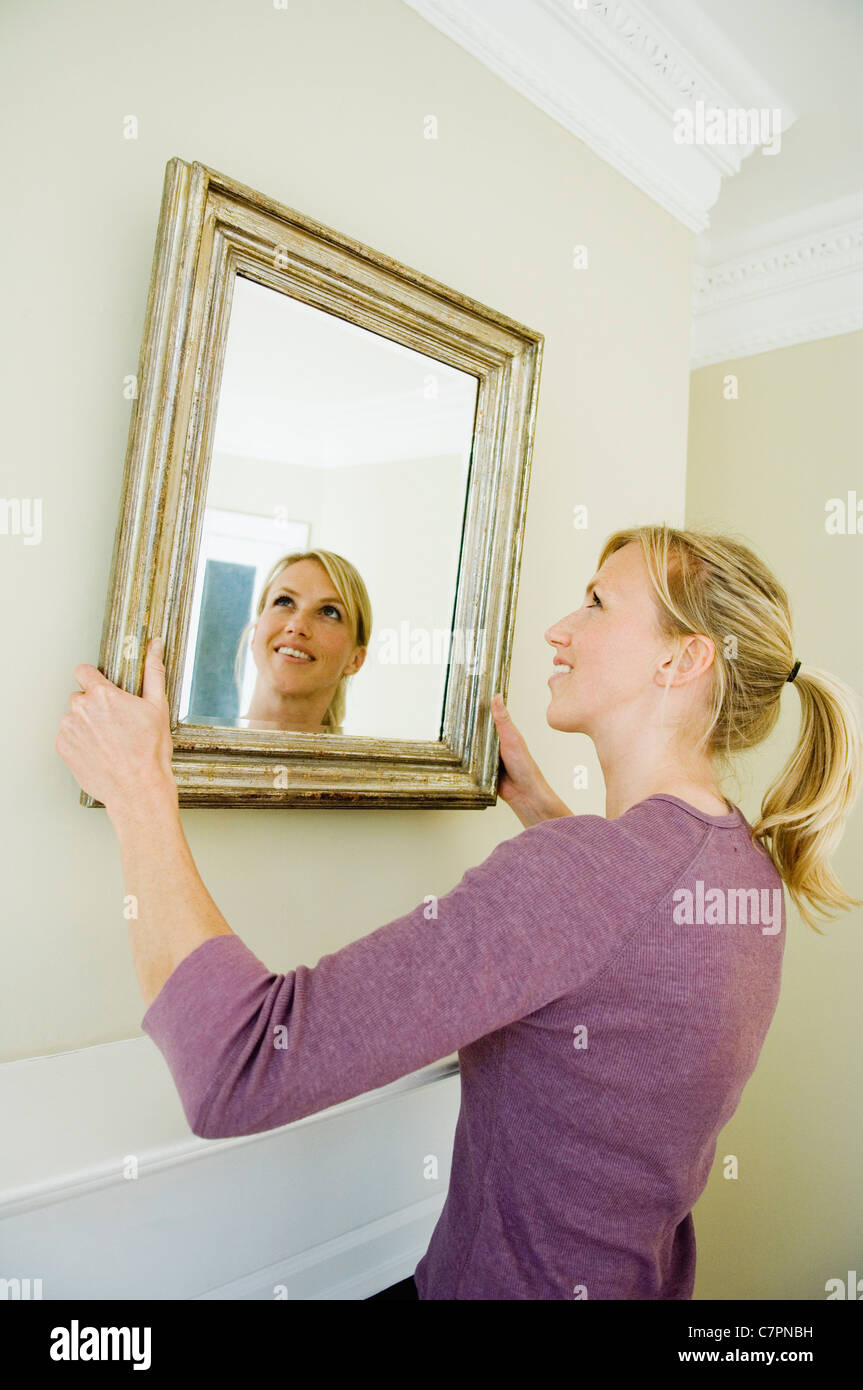 Woman hanging miroir sur le mur Banque D'Images