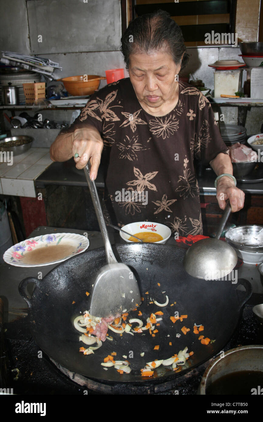 Femme chinoise sauté de légumes dans un wok dans un restaurant Indonésien Banque D'Images