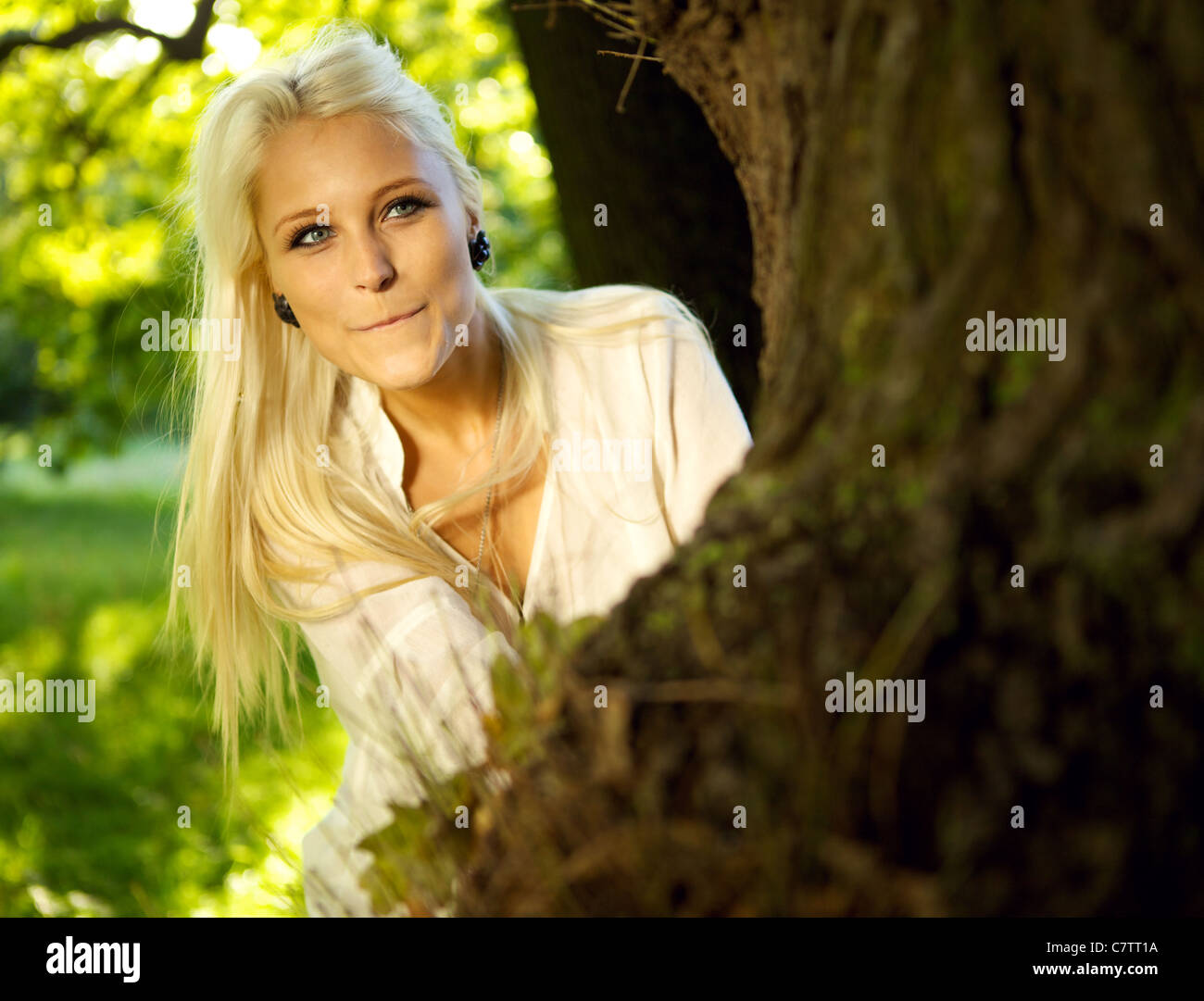 Jolie femme joue à cache-cache dans un parc - se cacher derrière un arbre. Banque D'Images