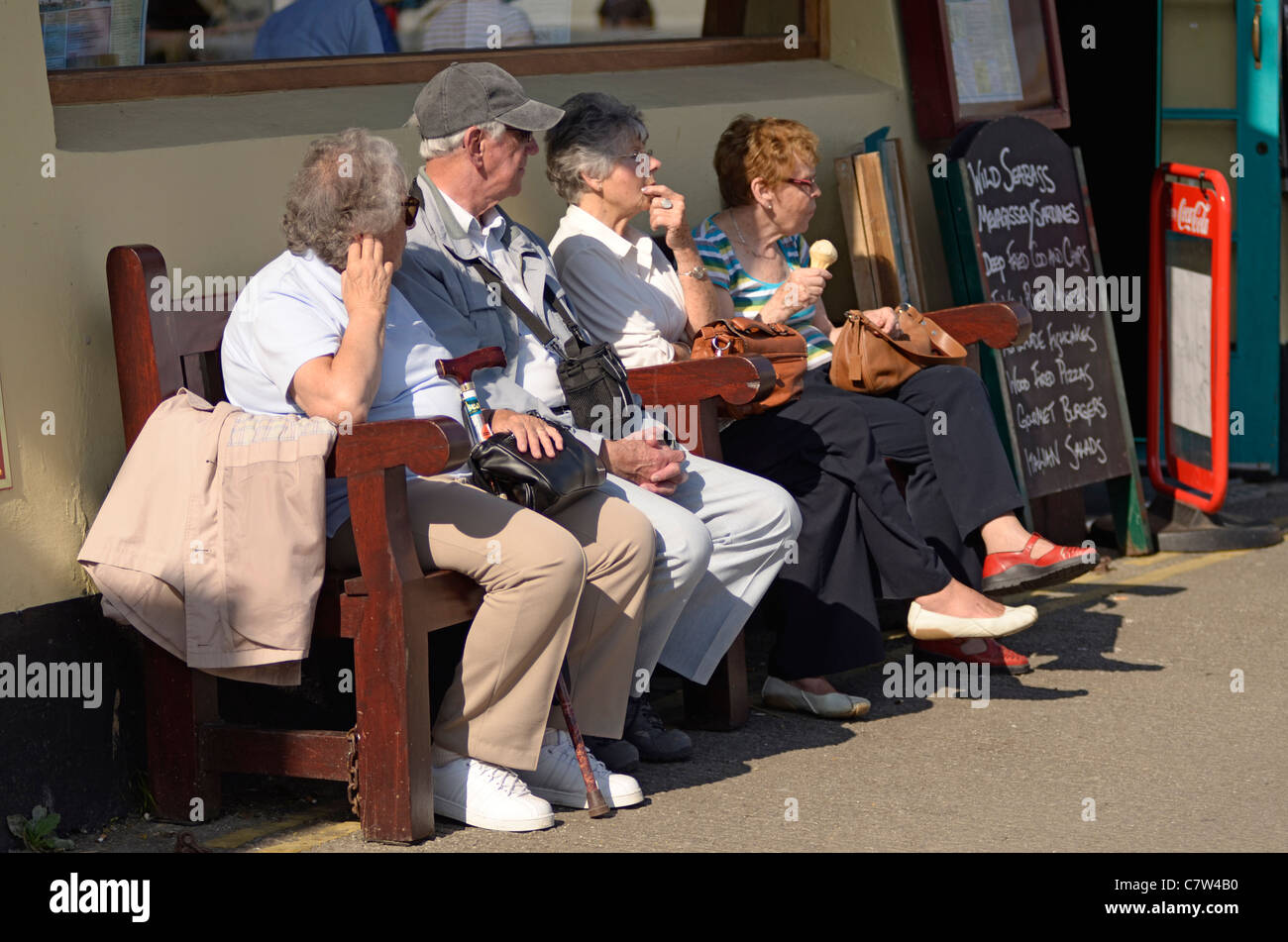 Couples retraités assis sur un banc à l'extérieur de pub à Mevagissey Cornwall UK Banque D'Images