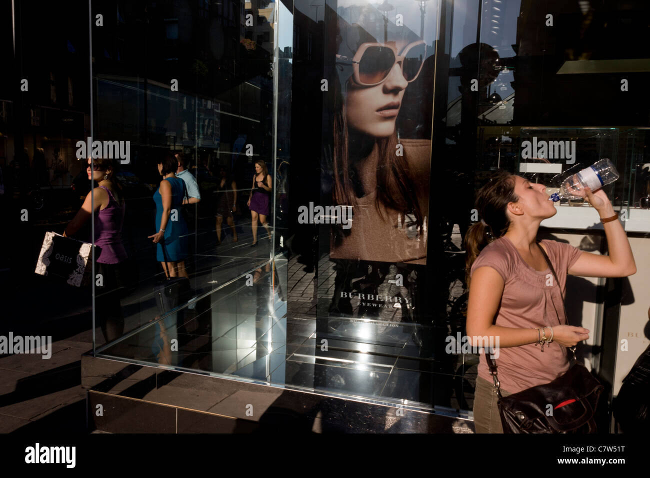 Une femme assoiffée finit sa bouteille d'eau par une affiche pour fille lunettes de soleil Burberry lunettes qu'ils appellent, dans une rue de Londres. Banque D'Images