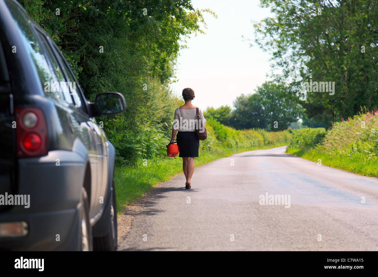 Photo d'une femme qui est en panne de véhicule marchant le long d'une route de campagne avec un carburant de rechange peut dans sa main. Banque D'Images
