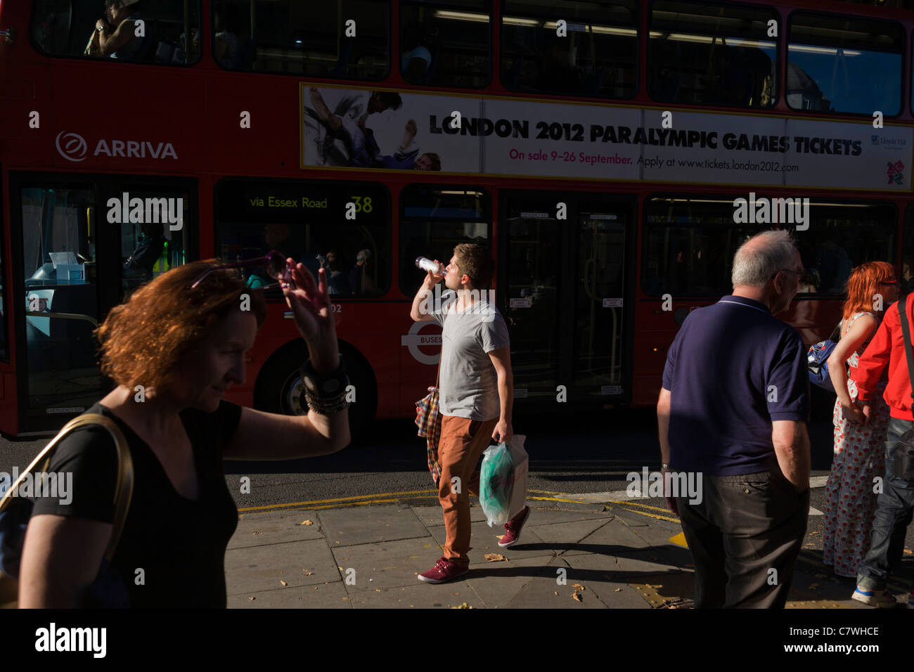 Homme boit de l'eau bouteille tandis que marcher le long de la rue de Londres aux côtés d'un London bus rouge avec aux Jeux paralympiques 2012 ad. Banque D'Images