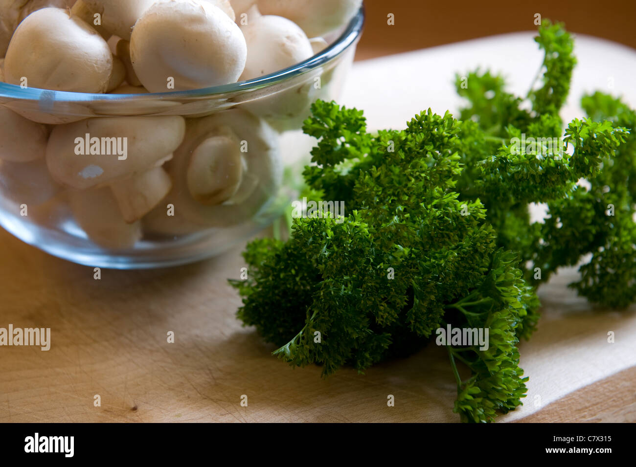 Les champignons dans un bol en verre parsley on a wooden ennuyer prêt à cuire Banque D'Images