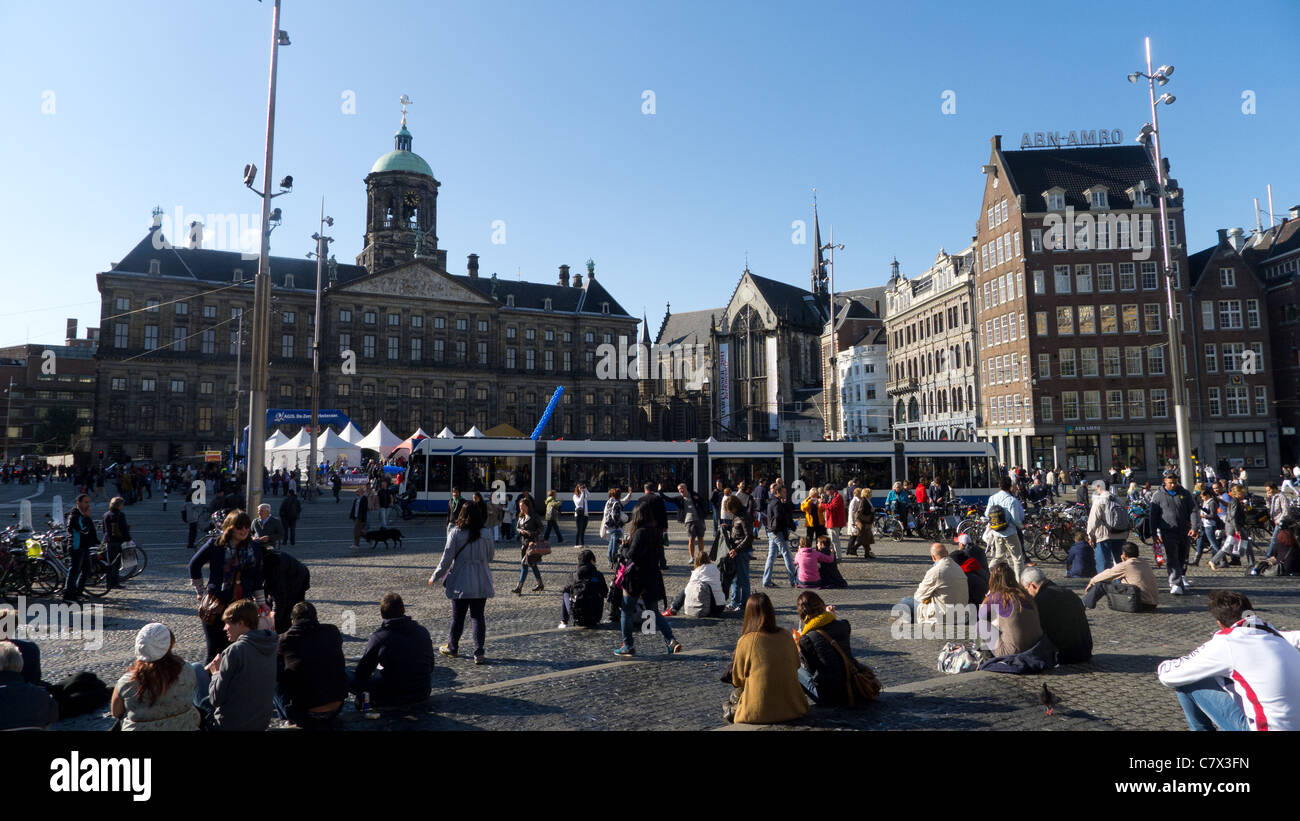 Les gens assis à la place du Dam avec un tramway en face du Palais Royal (Koninklijk Paleis), Amsterdam, Pays-Bas. Banque D'Images