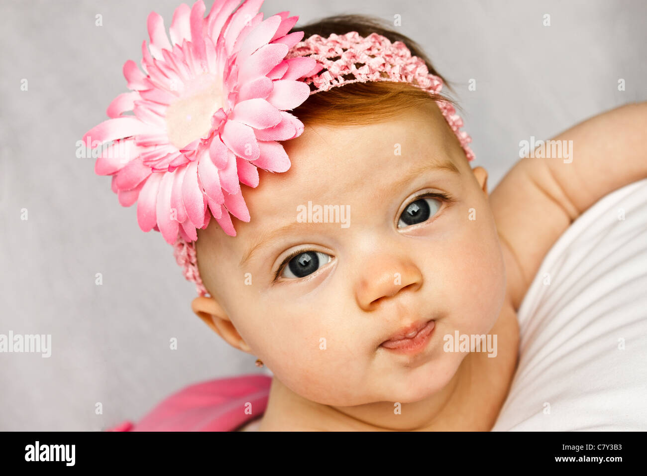 Adorable bébé fille aux yeux brillants qui posent avec une fleur rose band Banque D'Images