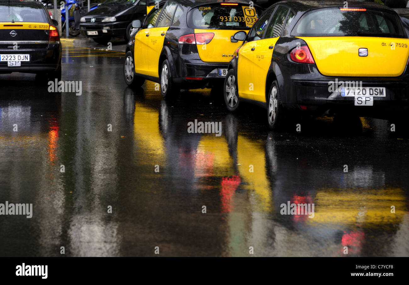 Les taxis jaune et noir catalan à Barcelone, Espagne avec leur couleur reflétée dans les routes humides et pluvieuses. Banque D'Images