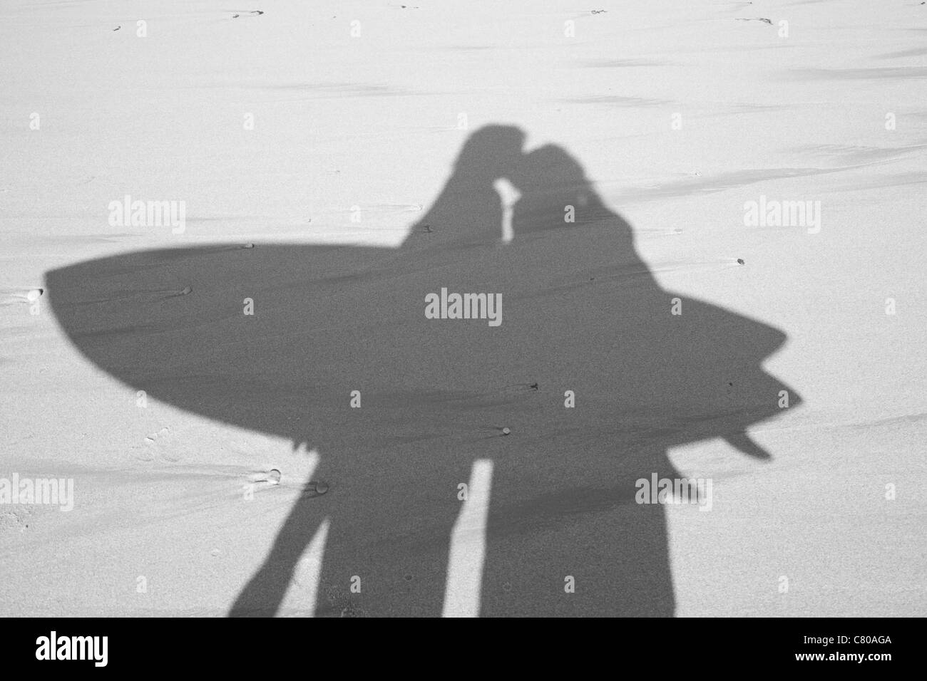 Photo en noir et blanc d'une ombre sur le sable d'un couple et de transporter une planche de surf. Banque D'Images